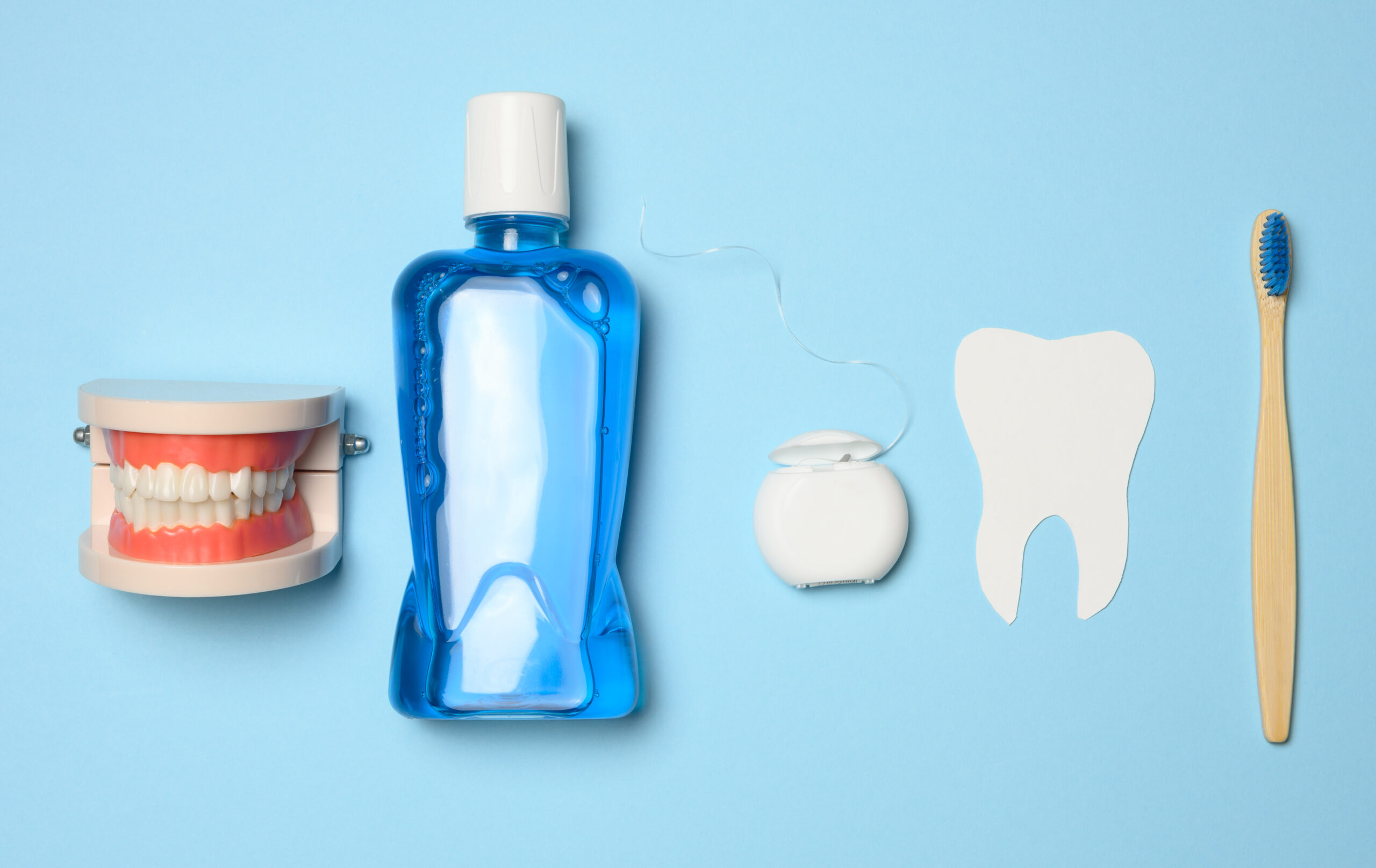 Oral hygiene essentials including a toothbrush, mouthwash, dental floss, tooth model, and a tooth cutout on a blue background.